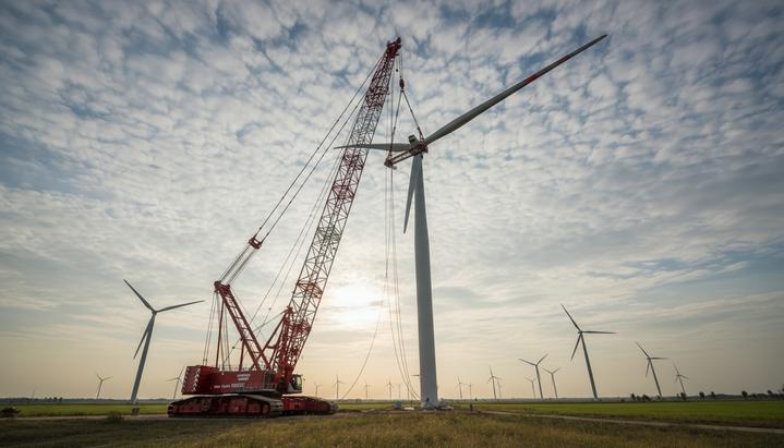 Огромный гусеничный кран поднимает гигантскую лопасть для установки на высокую ветряную турбину на ветроэлектростанции.