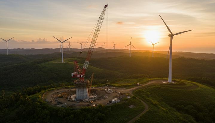 Ветряные турбины на зеленых холмах острова Лусон, Филиппины. Рядом с одной из турбин стоит строительный кран.