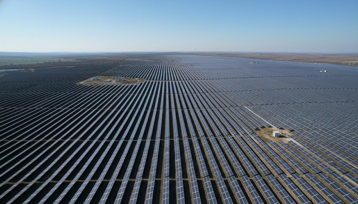 Бескрайние ряды солнечных панелей на электростанции Studina в Румынии, уходящие к горизонту под ясным небом.